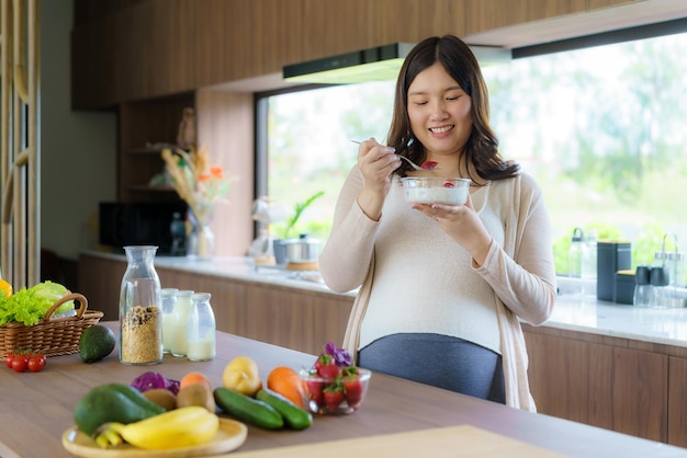 Bela mulher grávida asiática comendo com cereais de luxúria no café da manhã na cozinha em casa