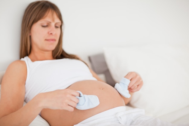 Bela mulher grávida brincando com pequenas meias enquanto deita em uma cama