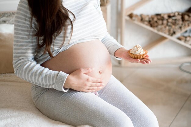 Foto bela mulher grávida comendo delicioso bolo doce em casa.