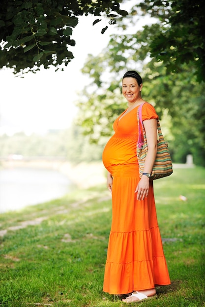 bela mulher grávida feliz ao ar livre na natureza brilhante em vestido laranja