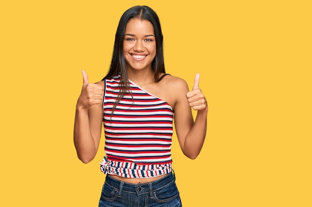 Bela mulher hispânica vestindo roupas casuais sinal de sucesso fazendo gesto positivo com a mão polegares para cima sorrindo e feliz expressão alegre e gesto de vencedor