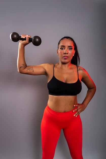 Foto bela mulher morena em roupas de ginásio segurando halteres pretos à altura da cabeça vida saudável.