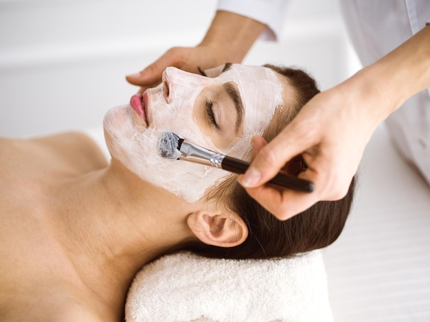 Bela mulher morena gostando de aplicar máscara cosmética confortável e bissfulle. Tratamento relaxante em medicina e conceitos de centro de spa.