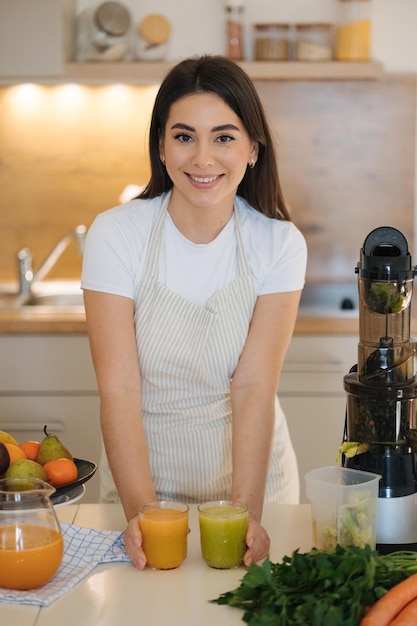 Foto bela mulher na cozinha terminar fazer um suco fresco dois copos de bebidas diferentes no