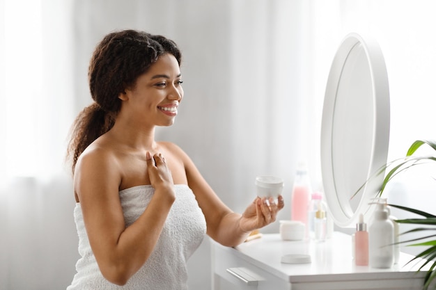 Foto bela mulher negra aplicando creme na zona de decolte em casa