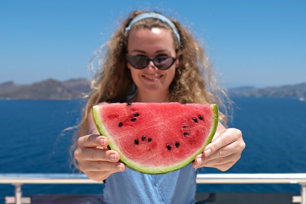 Bela mulher sorridente com uma fatia de melancia vestindo maiô com vista para o mar no fundo. férias de verão.