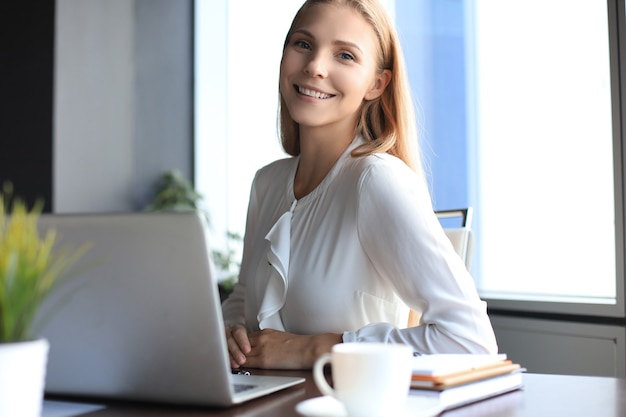 Bela mulher sorridente de negócios está sentada no escritório e olhando para a câmera.