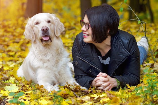 Bela mulher sorridente morena com golden retriever no outono park.