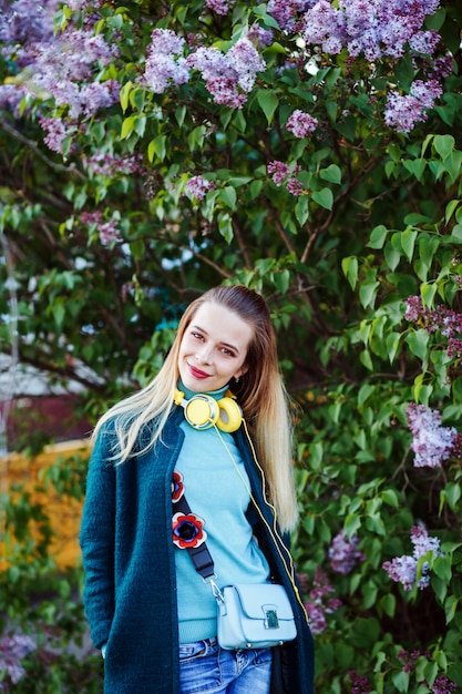 Bela mulher sorridente usando fones de ouvido amarelos sob o arbusto lilás