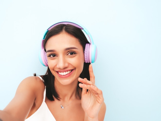 Bela mulher sorridente, vestida de pijama branco. modelo despreocupado ouvindo música em fones de ouvido sem fio