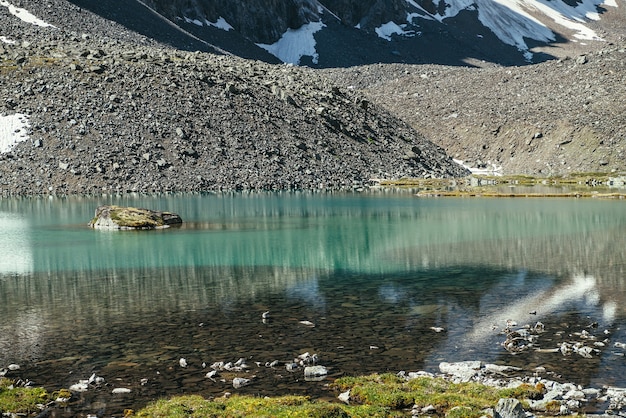Bela paisagem cênica com lago de montanha turquesa com água transparente e fundo pedregoso. Lago glacial azul com superfície de água clara na luz solar. Neve branca e grama verde perto do lago de montanha.