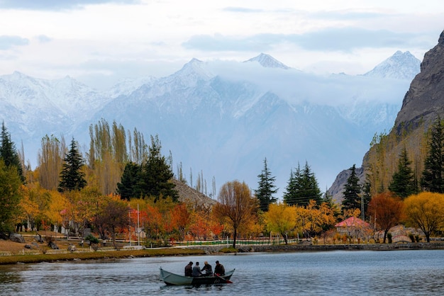 bela paisagem com barco em árvores de outono do lago e montanhas de neve ao fundo