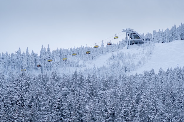 Bela paisagem de floresta de montanha de inverno com pessoas levantando em um teleférico