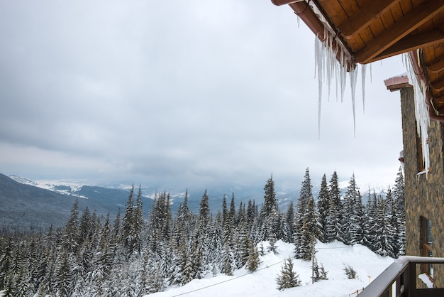 Bela paisagem de inverno com altos pinheiros e montanhas filmadas da varanda de um chalé com pingentes de gelo