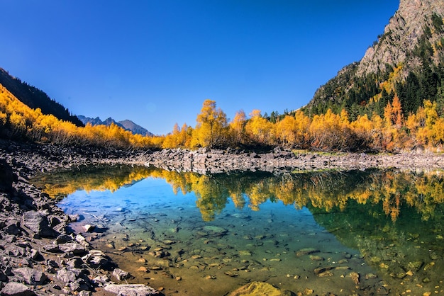 Bela paisagem de outono com água verde clara de um lago de montanha e árvores refletidas com folhagem de outono e picos de montanha