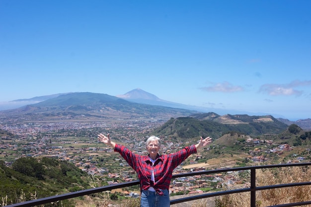 Bela paisagem do vulcão El Teide na ilha de Tenerife mulher idosa caucasiana em pé com os braços estendidos aproveitando as férias expressando alegria e liberdade