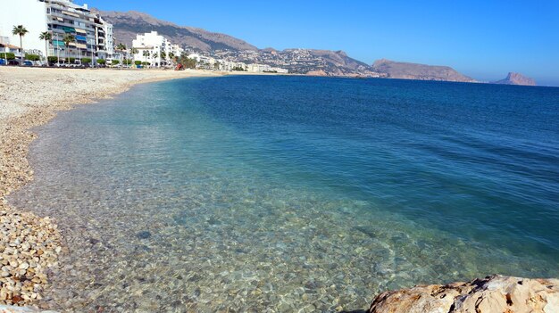 Bela paisagem marinha, mar azul claro, pebble beach, casas brancas à distância, montanhas, mediterrâneo