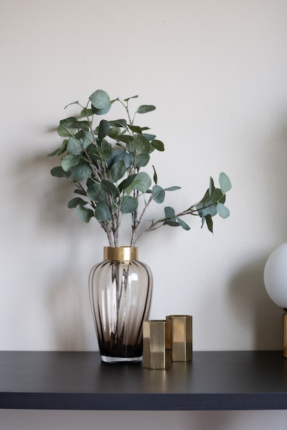 Bela planta artificial em vaso de vidro com borda de ouro inoxidável e vaso de espelho de ouro e ajuste de lâmpada no tampo da mesa de madeira preto vazio.
