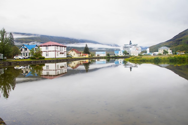 Bela reflexão de casas, igreja, rodovia e estrada de arco-íris na cidade de Seydisfjordur, na Islândia