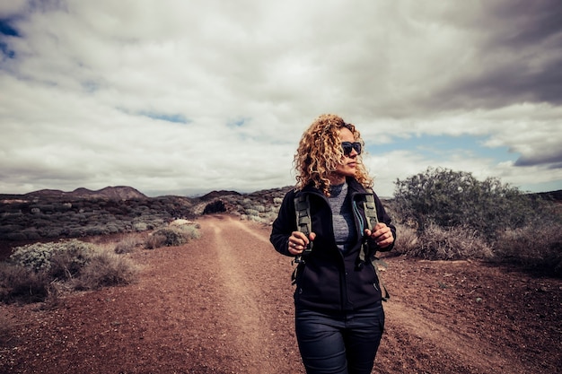 Foto bela trekker caucasiana loira encaracolada jovem ativa caminhar no caminho do deserto, desfrutando da liberdade e do estilo de vida ativo, viajando com uma mochila sozinha no parque natural ao ar livre