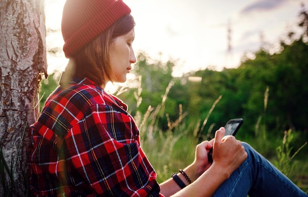 Bela viajante feminina sentada perto da árvore e digitando no celular