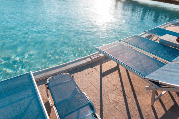 Bela vista da piscina com água azul e espreguiçadeira de praia ao pôr do sol. Conceito de relaxamento, natação e saúde