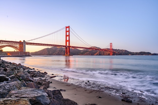 Bela vista da Ponte Golden Gate na Califórnia, EUA, pela praia rochosa com o céu ao pôr-do-sol