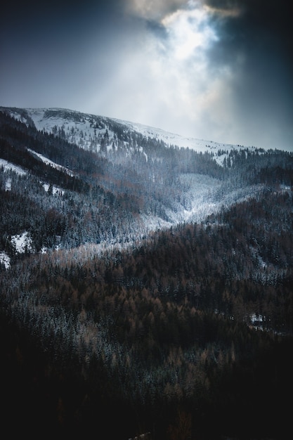 Bela vista do sol brilhando através das nuvens sobre altas montanhas nevadas