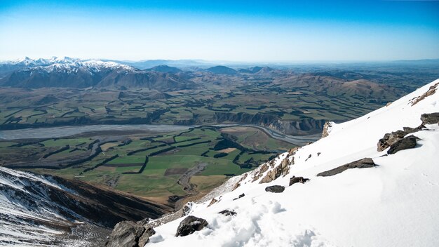 Bela vista do topo da montanha nevada até o vale verde com montanhas ao fundo e céu azul