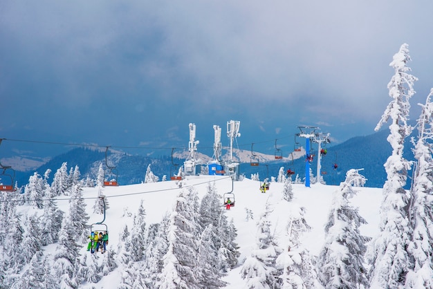 Bela vista inferior dos funiculares localizados acima de uma pitoresca encosta coberta de neve com árvores em um dia nublado de inverno.