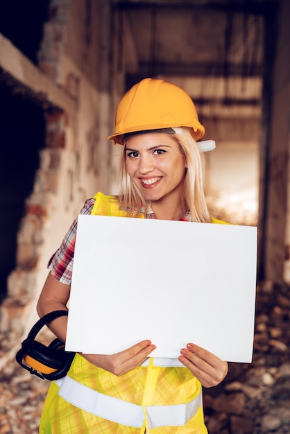 Belas jovens arquitetos de construção feminina segurando um quadro branco em branco no edifício danificado no desastre.