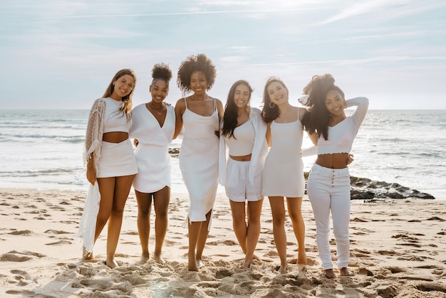 Belas jovens multirraciais posando na praia perto do oceano tendo uma festa de despedida de solteiro