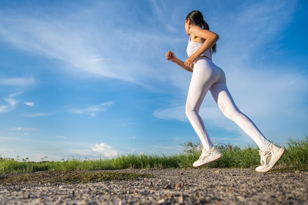 Belas mulheres asiáticas em roupas esportivas correndo na grama verde com céu azul ao fundo, prontas para exercícios ao ar livre. Conceito de mulheres saudáveis. Treino de corrida.