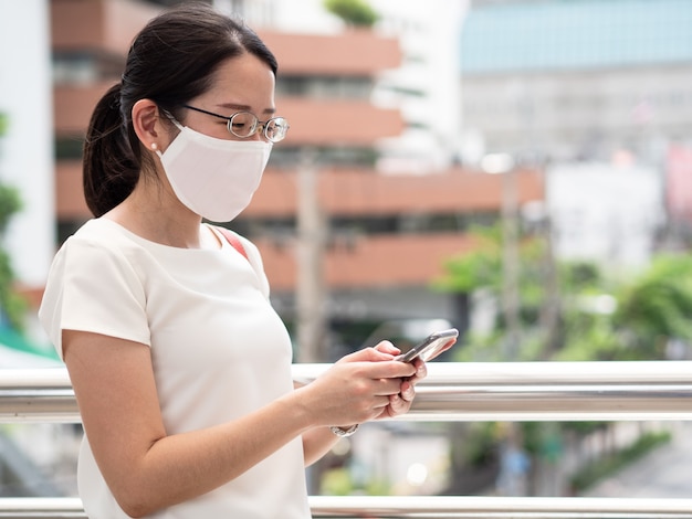 Foto belas mulheres asiáticas usando máscara médica descartável, usando smartphone em áreas públicas, na estrada ou no centro da cidade, como nova tendência normal e autoproteção contra a infecção covid19.