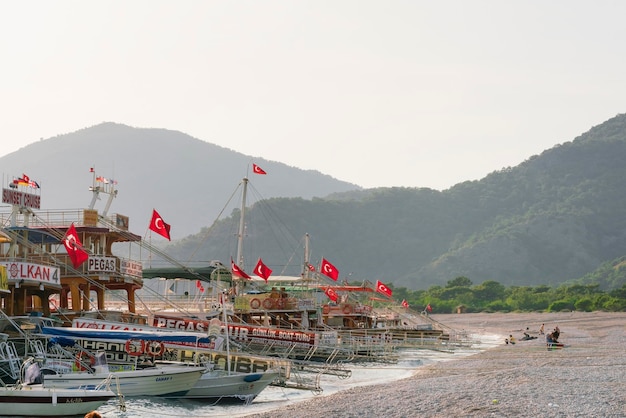 Belas vistas da praia da marina com pessoas e barcos de recreio com placas publicitárias e bandeiras turcas sobre um fundo de montanhas
