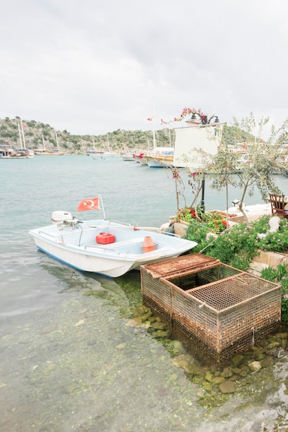 Belas vistas do barco a motor branco da marina com bandeira turca atracada na costa com os canteiros de flores perto da grelha metálica enferrujada