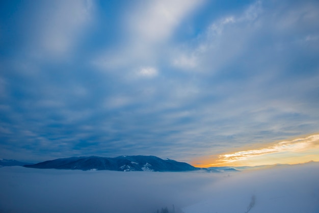 Belas vistas mágicas dos picos das montanhas estão localizadas entre a névoa e as nuvens cirros em uma noite quente de outono contra o pôr do sol