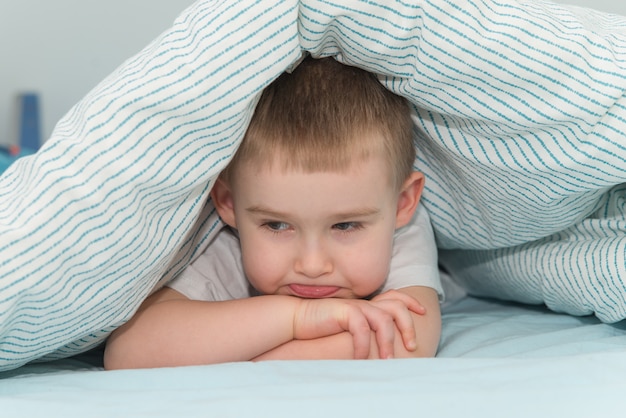 Beleidigter kleiner Junge liegt unter der Decke und schaut nach unten