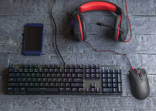 Beleuchtete Gaming-Tastatur, Kopfhörer und Maus auf einem Holztisch