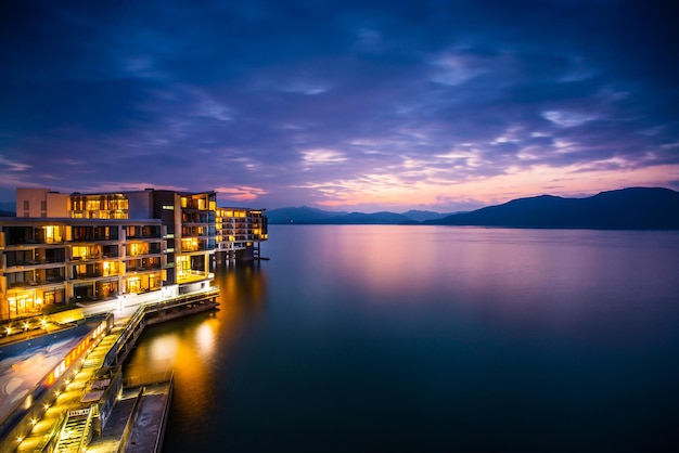 Beleuchtetes Hotel am See gegen den bewölkten Himmel in der Dämmerung
