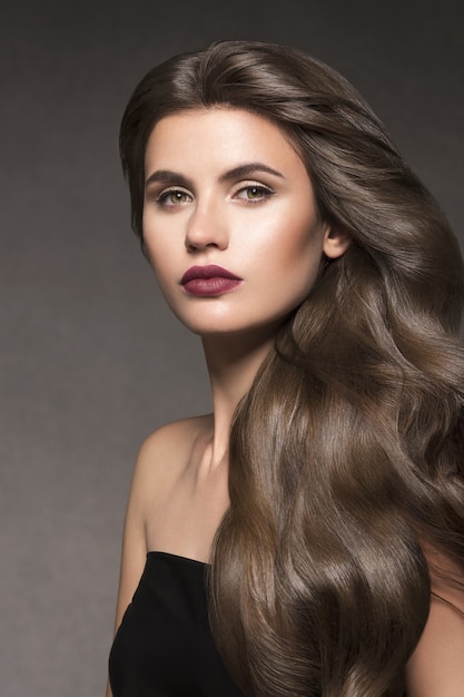 Beleza cabelo mulher retrato longo encaracolado penteado moda maquiagem pele saudável. Fundo escuro.