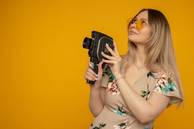 Foto beleza com câmera de filme. jovem alegre segurando uma câmera de filme e posando contra um fundo amarelo