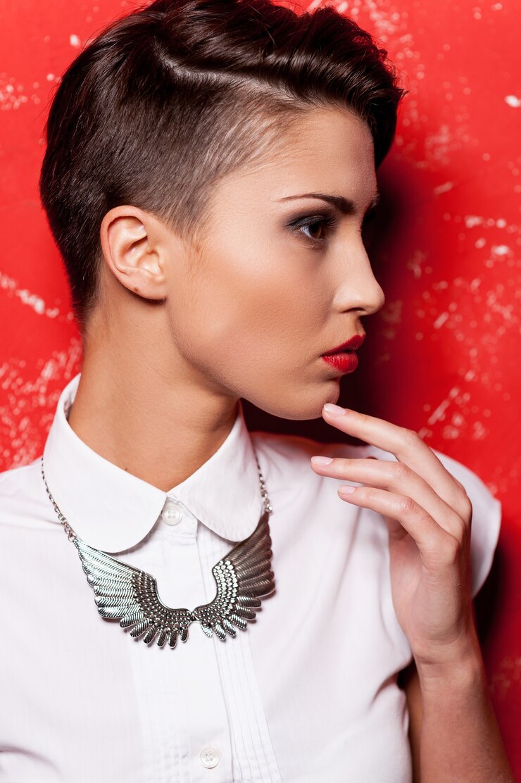 Foto beleza com penteado elegante. vista lateral de uma mulher jovem e bonita de cabelo curto em camisa branca, segurando a mão no queixo em pé contra um fundo vermelho