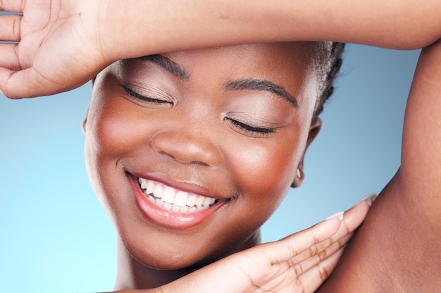 Beleza cuidado da pele e mulher negra close-up de axila e sorriso cosméticos e maquiagem em estúdio bem-estar feliz modelo africano em fundo azul e pele brilho com brilho de tratamento de dermatologia