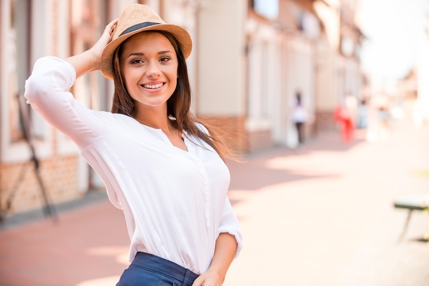 Beleza da moda. Mulher jovem e bonita ajustando o chapéu e sorrindo ao ar livre