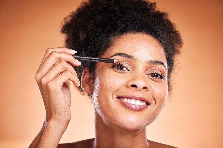 Foto beleza de delineador e retrato de uma mulher negra fazendo uma rotina de maquiagem cosmética no estúdio cosméticos linda e feliz modelo africana fazendo maquiagem nos olhos com lápis isolado por fundo laranja