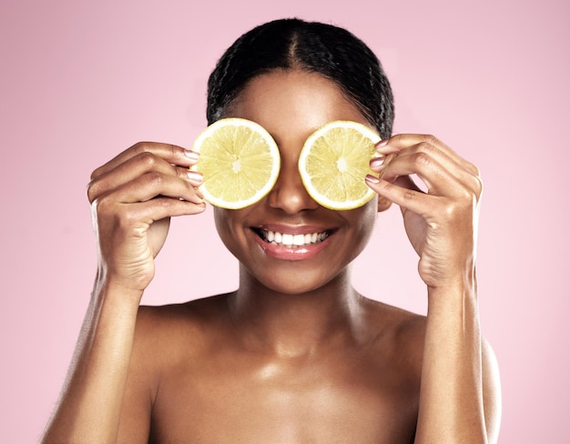 Beleza de mulher feliz e olhos com limão no fundo rosa do estúdio e benefícios da vitamina c Modelo africano de rosto e diversão com frutas cítricas para cuidados com a pele naturais cosméticos veganos e estética facial