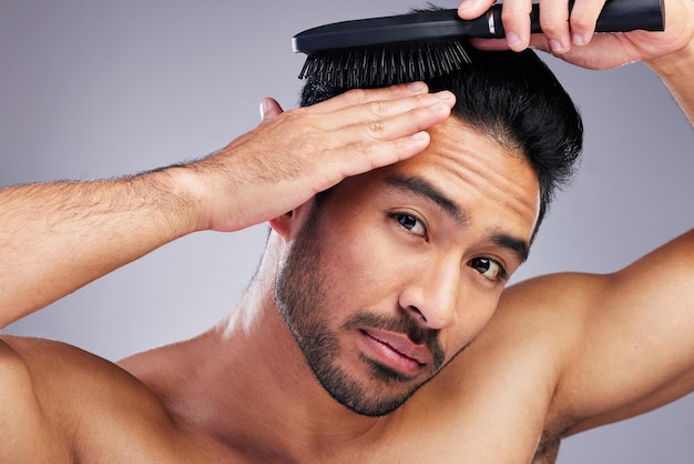 Beleza de retrato ou homem escovando o cabelo em aliciamento com produto de cuidado de cabelo de salão no fundo do estúdio Escova de pessoa natural ou modelo masculino asiático saudável e confiante com penteado legal na rotina matinal