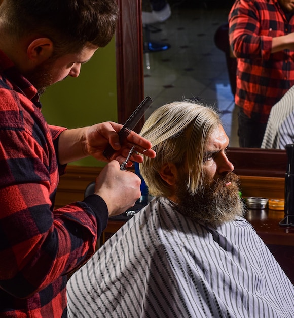 Beleza e moda Retrato de barbear de homem elegante barbear cabeleireiro na barbearia homem no salão de cabeleireiro com barba e bigodes de corte de cabelo hipster Cabeleireiro profissional no interior da barbearia