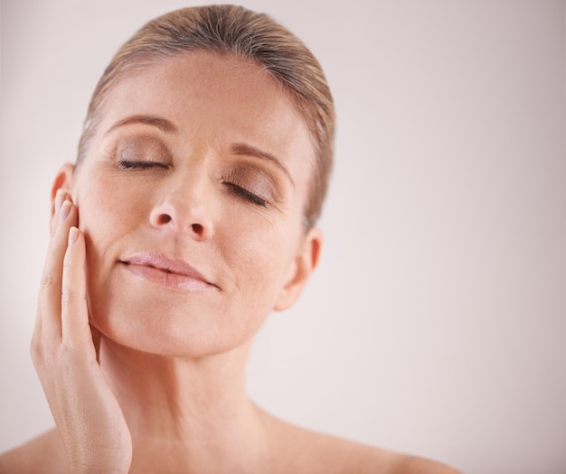 Beleza facial e maquete com uma mulher madura no estúdio em um fundo de maquete para tratamento antienvelhecimento natural Cuidados com a pele facial e bem-estar com uma atraente modelo idosa tocando sua bochecha